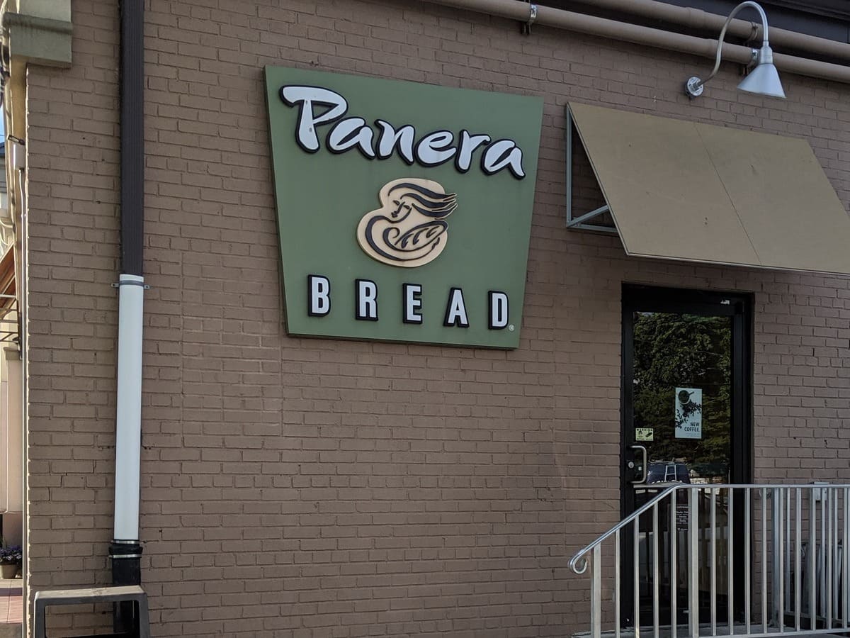 A panera bread sign is on the front of a brick building.