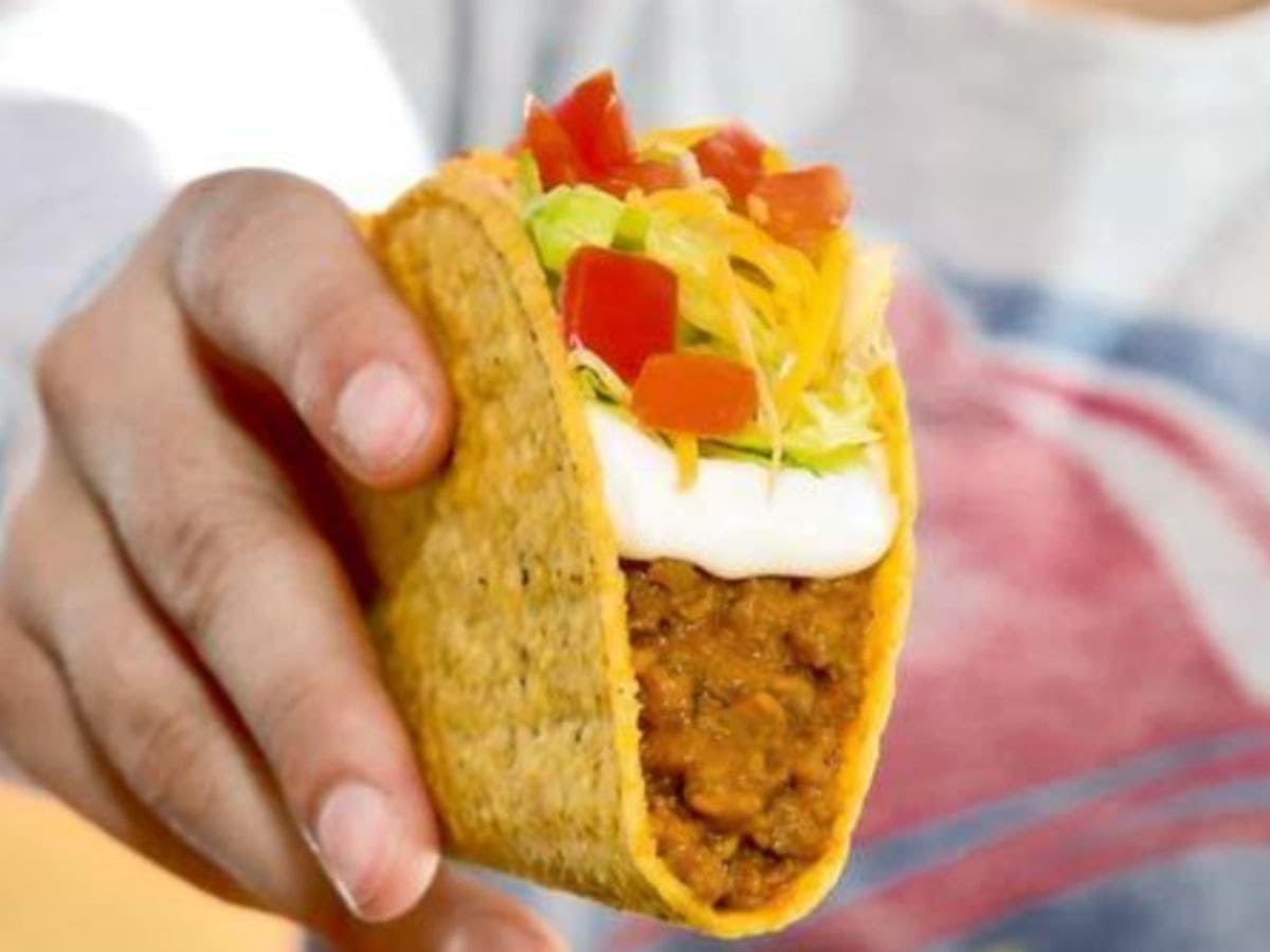 A person is holding up a high-protein taco with toppings.