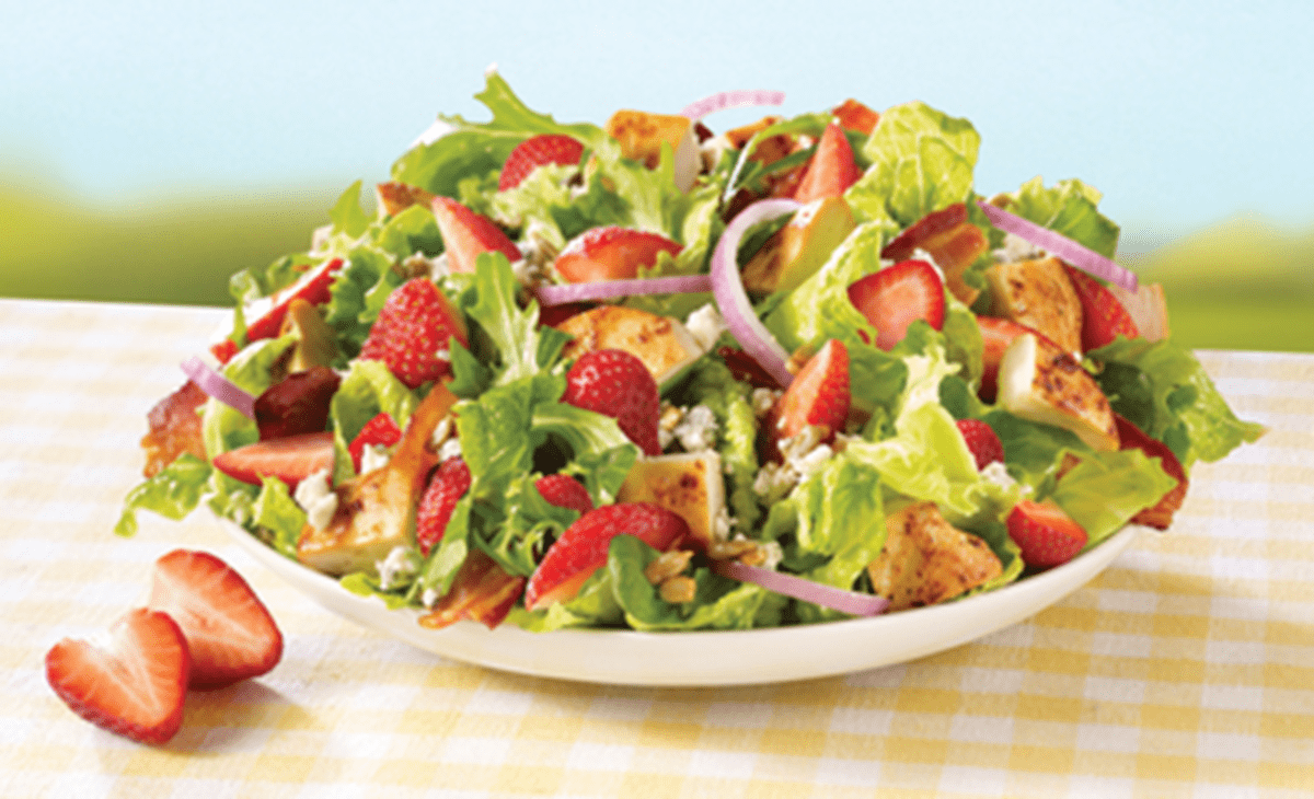 A bowl of salad with strawberries, onions and bacon.