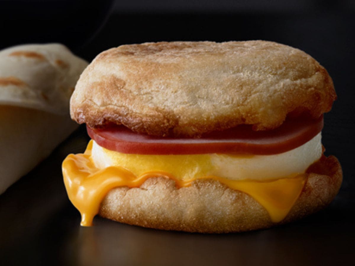 A fast food breakfast sandwich with ham and cheese on a plate.