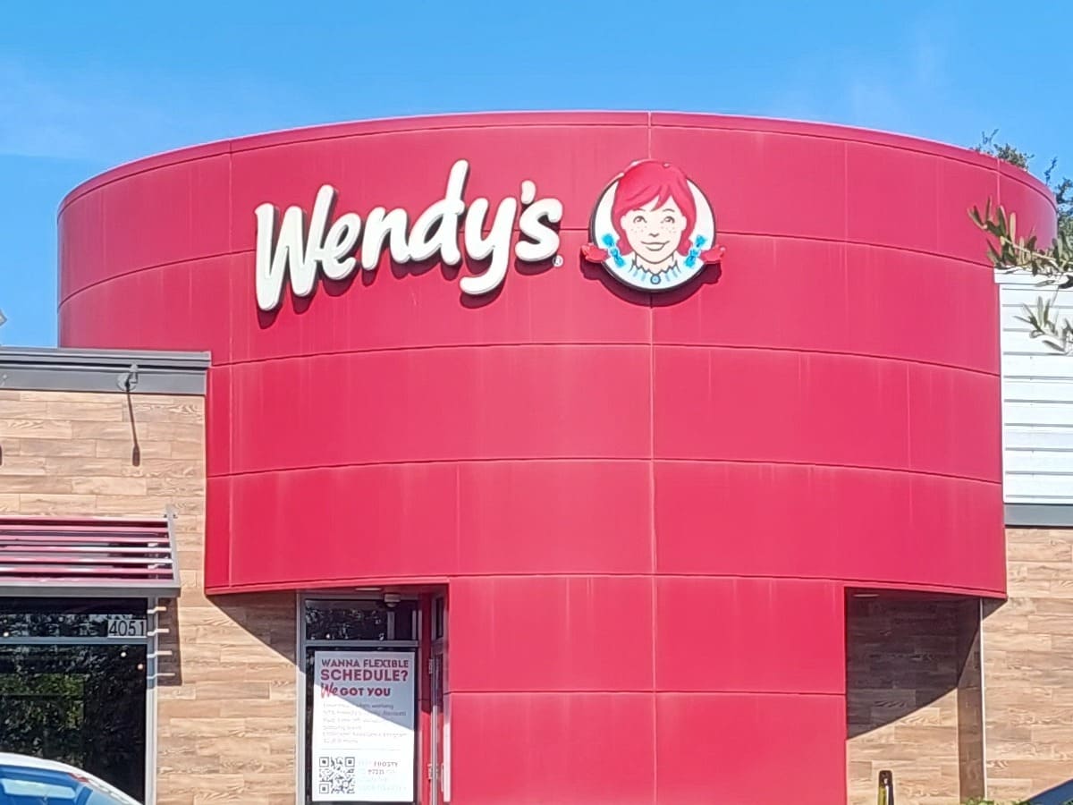 A heart-healthy Wendy's restaurant with cars parked in front of it.